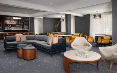Lobby lounge with gray sectional sofa, upholstered armchairs, round wooden coffee tables and a nearby refreshment counter at Courtyard By Marriott Dothan.