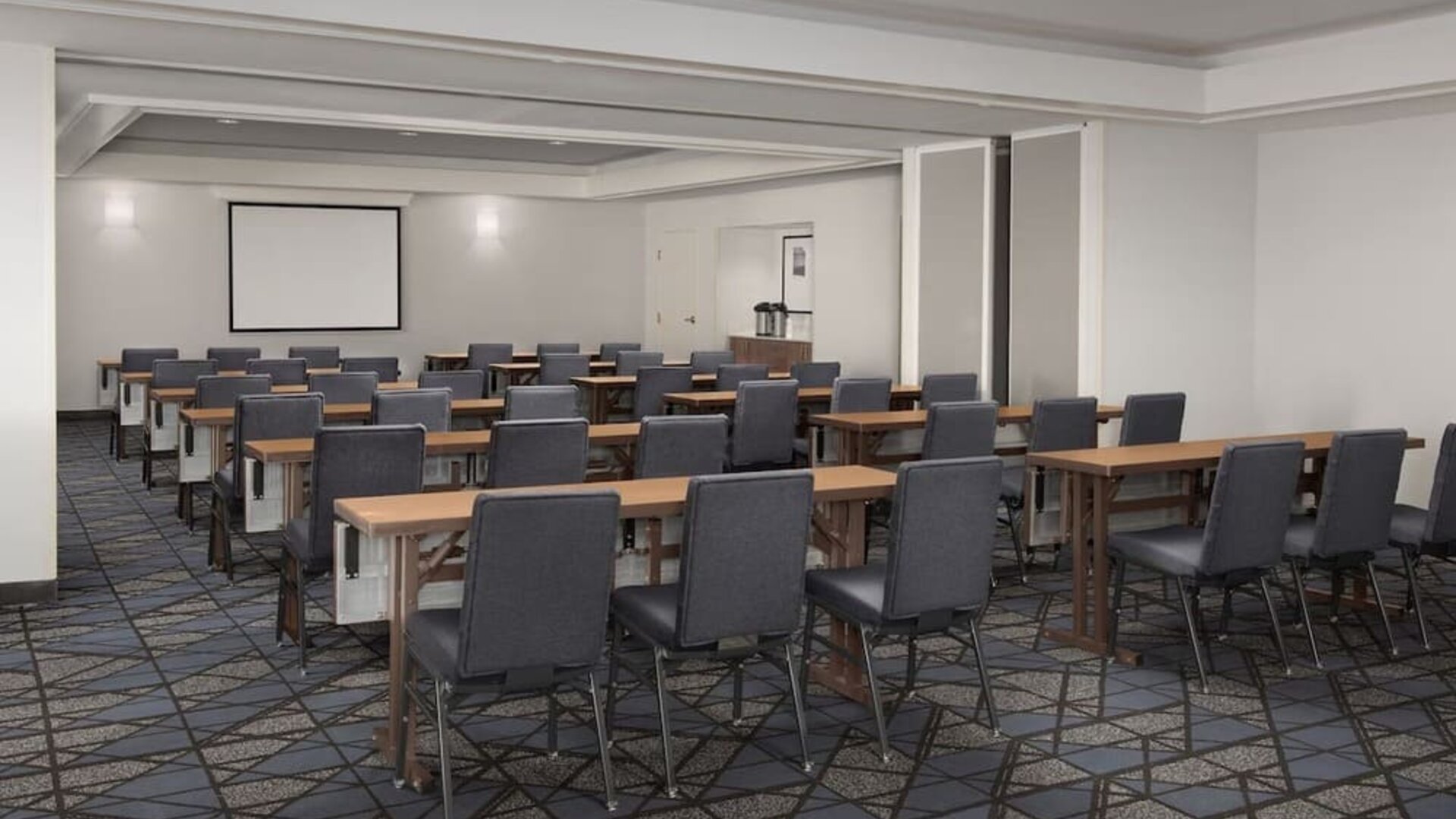 Meeting room arranged classroom-style with rows of tables, gray chairs, patterned carpet and a projection screen at Courtyard By Marriott Dothan.