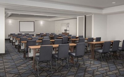 Meeting room arranged classroom-style with rows of tables, gray chairs, patterned carpet and a projection screen at Courtyard By Marriott Dothan.