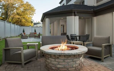 Outdoor patio with cushioned lounge chairs surrounding a circular brick fire pit, with lawn and landscaping at Courtyard By Marriott Dothan.