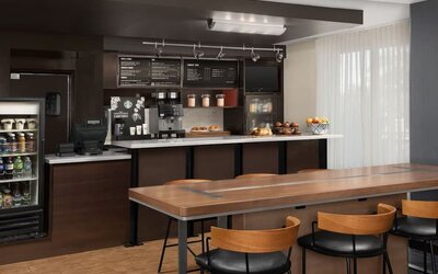 Refreshment station with coffee machines, refrigerated drinks, pastries, fruit and a long communal wooden table at Courtyard By Marriott Dothan.