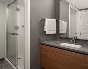 Bathroom with glass shower enclosure, wall-mounted showerhead, gray vanity countertop, inset sink and folded white towels at Courtyard By Marriott Dothan.