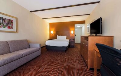 Guest room with king bed, grey sofa, wooden dresser, television and desk on striped carpet at Best Western Executive Hotel Of New Haven-West Haven.