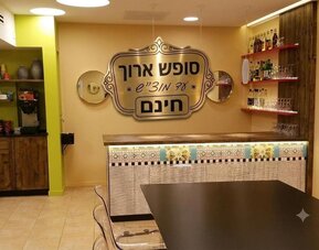 Hotel bar area with patterned counter, wooden shelves, glassware and a large Hebrew sign at Mizpe Yam Netanya Boutique Hotel.
