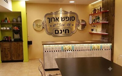 Hotel bar area with patterned counter, wooden shelves, glassware and a large Hebrew sign at Mizpe Yam Netanya Boutique Hotel.