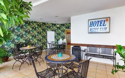 Hotel seating area with round mosaic tables, wrought-iron chairs, leafy wallpaper and a wall sign at Mizpe Yam Netanya Boutique Hotel.