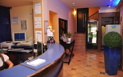 Reception area with curved blue counter, computer equipment, staircase and drinks refrigerator at Mizpe Yam Netanya Boutique Hotel.