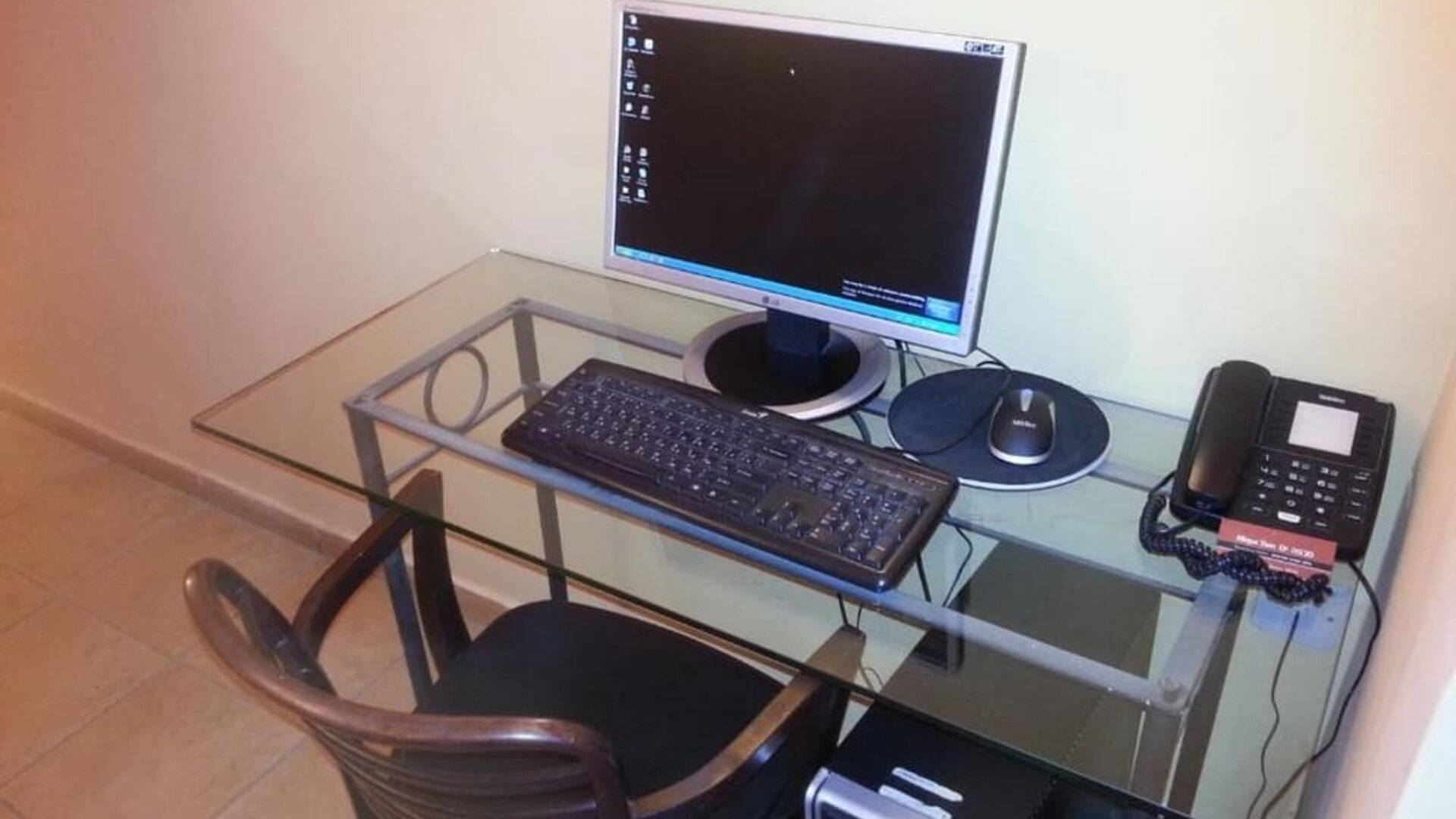 Workstation with glass desk, desktop computer, keyboard, telephone and wooden chair at Mizpe Yam Netanya Boutique Hotel.