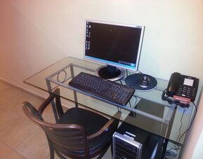Workstation with glass desk, desktop computer, keyboard, telephone and wooden chair at Mizpe Yam Netanya Boutique Hotel.