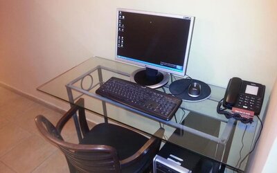 Workstation with glass desk, desktop computer, keyboard, telephone and wooden chair at Mizpe Yam Netanya Boutique Hotel.