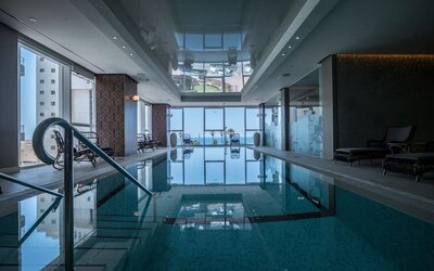 Indoor swimming pool with floor-to-ceiling windows, water views and dark wicker loungers at David Tower Hotel Netanya.