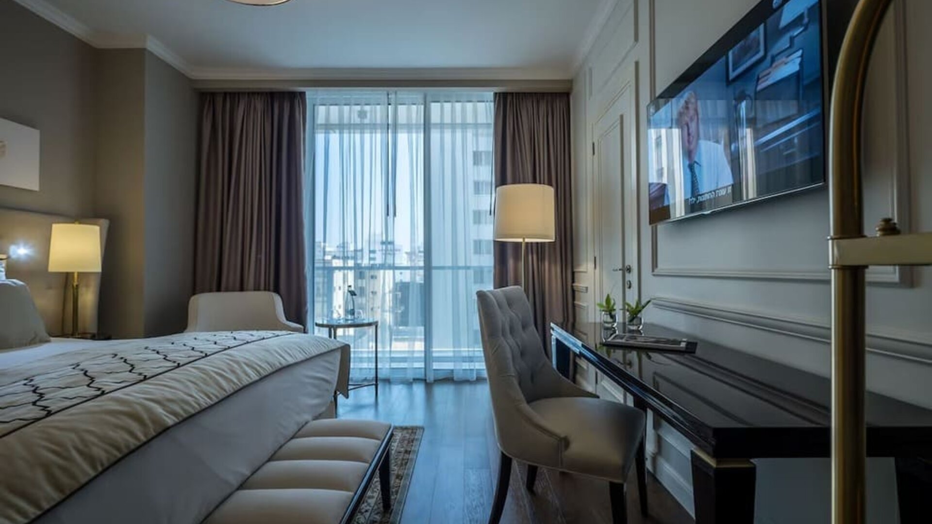 Guest room with king bed, upholstered chair, desk, wall-mounted television and balcony windows at David Tower Hotel Netanya.