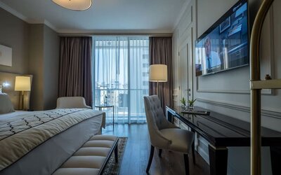 Guest room with king bed, upholstered chair, desk, wall-mounted television and balcony windows at David Tower Hotel Netanya.