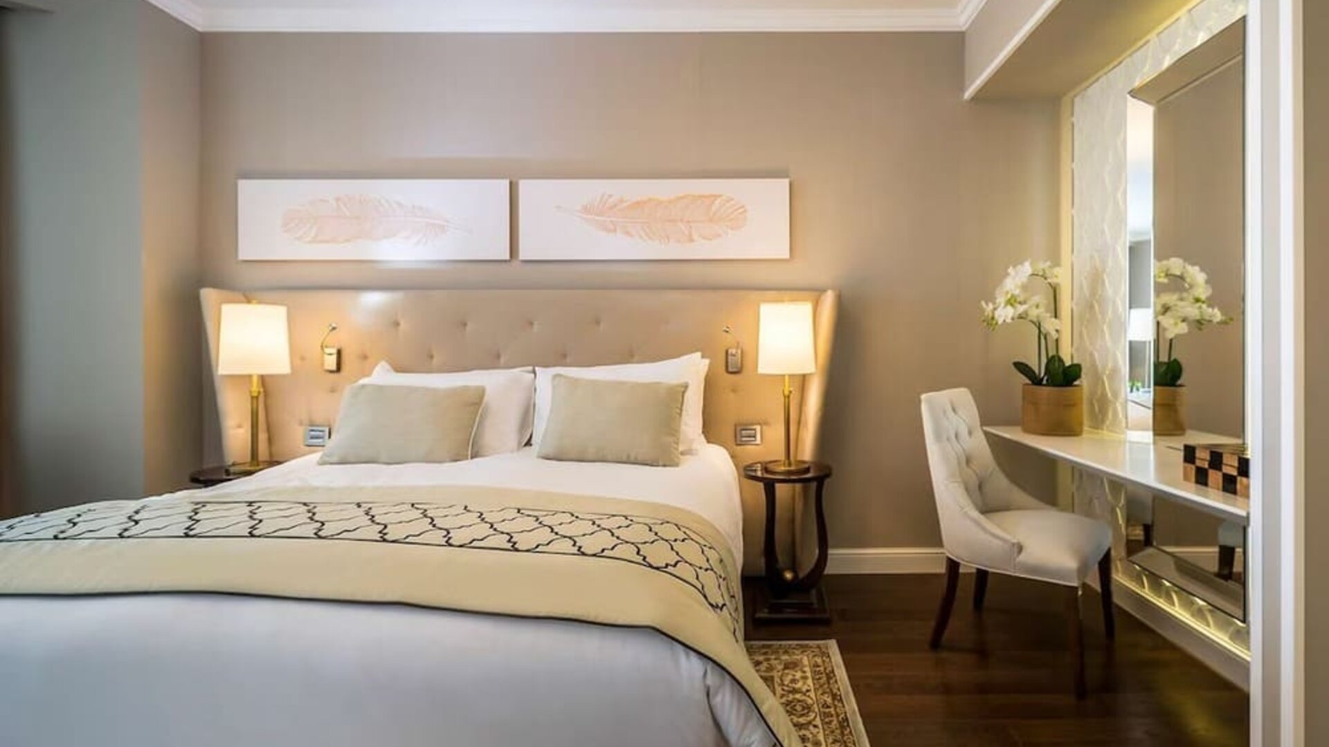Elegant guest room with king bed, upholstered headboard, bedside lamps and mirrored dressing desk at David Tower Hotel Netanya.