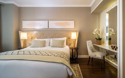 Elegant guest room with king bed, upholstered headboard, bedside lamps and mirrored dressing desk at David Tower Hotel Netanya.