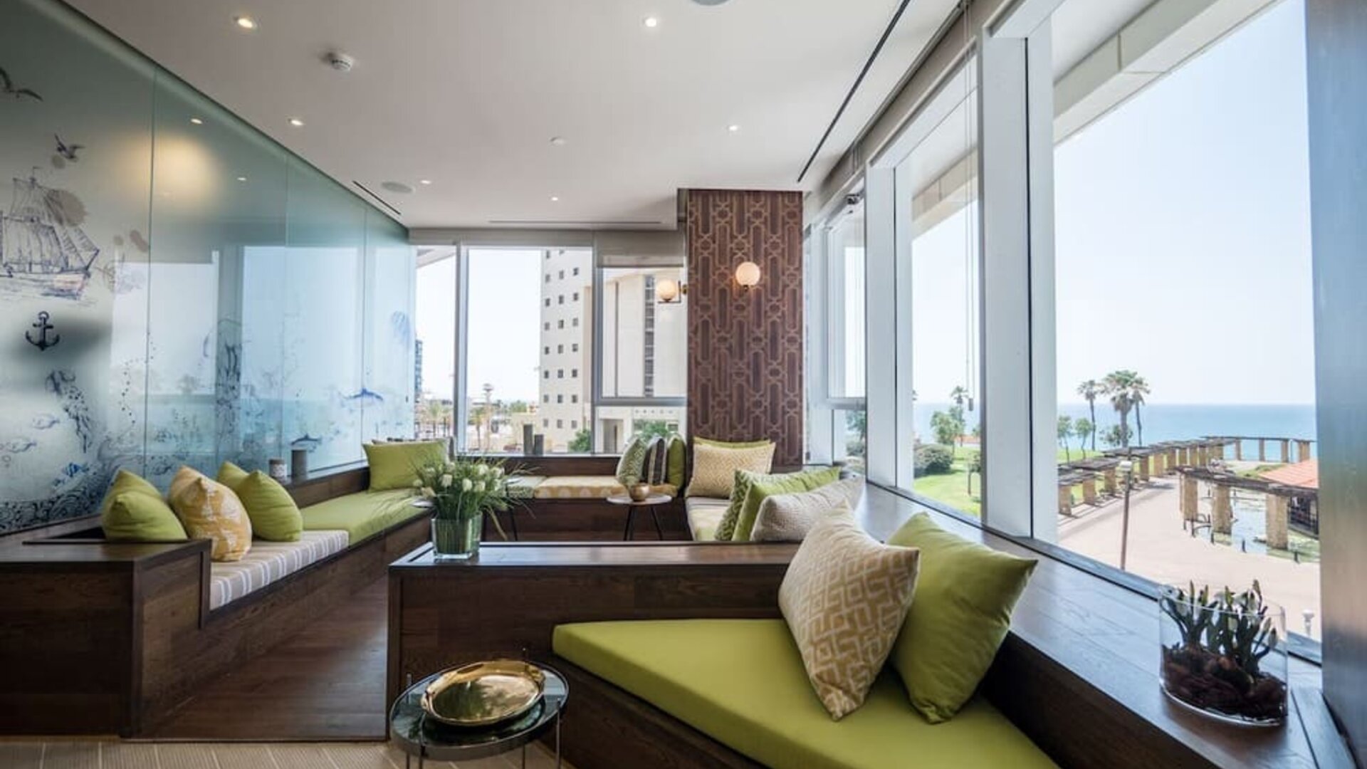 Window-side lounge with built-in green seating, patterned cushions and panoramic views of the sea at David Tower Hotel Netanya.