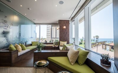 Window-side lounge with built-in green seating, patterned cushions and panoramic views of the sea at David Tower Hotel Netanya.