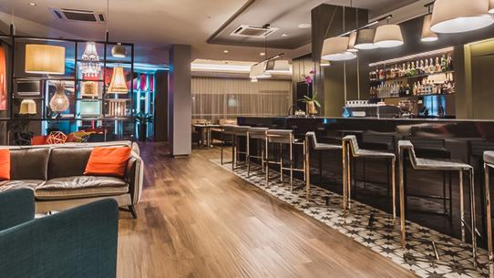 Hotel bar with dark leather sofas, colorful accent cushions, upholstered chairs, high stools and illuminated shelving at Novotel Lima San Isidro.