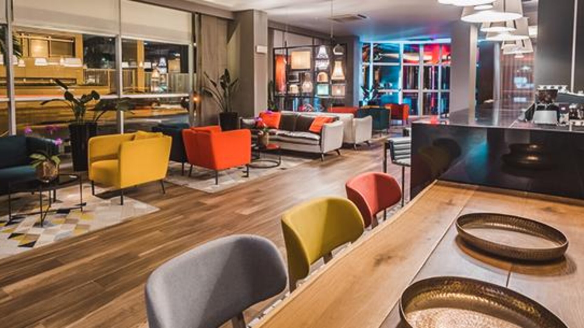 Hotel lounge and bar seating with colourful armchairs, sofas, pendant lights and a long communal table at Novotel Lima San Isidro.
