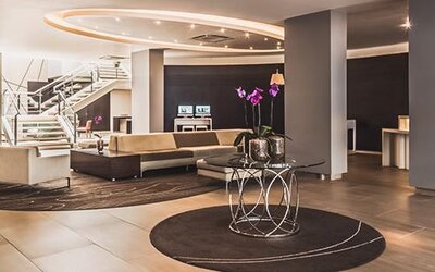 Spacious hotel lobby with cream sofas, circular rugs, decorative tables, staircase and reception area at Novotel Lima San Isidro.