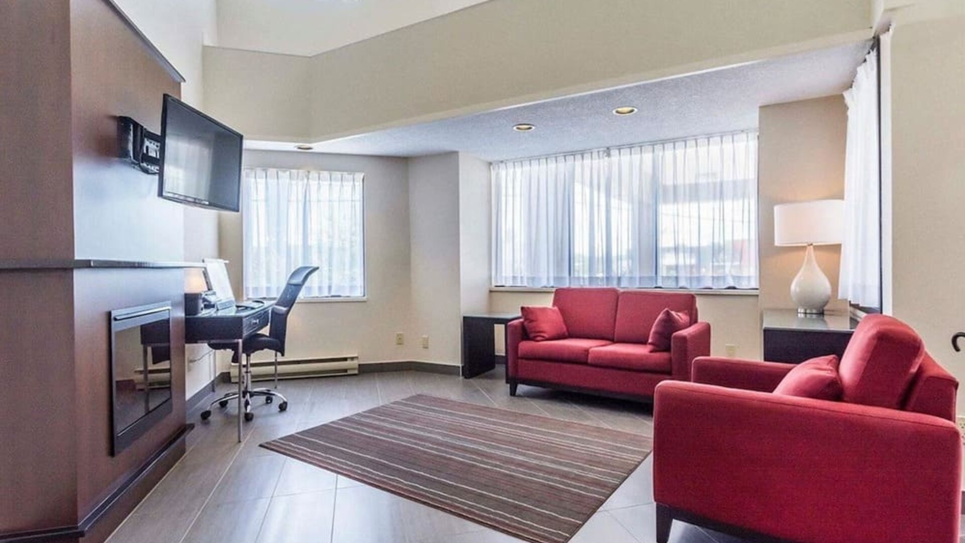 Lobby lounge area with fireplace and workspace with computer, printer and ergonomic chair at Comfort Inn Thetford Mines. 