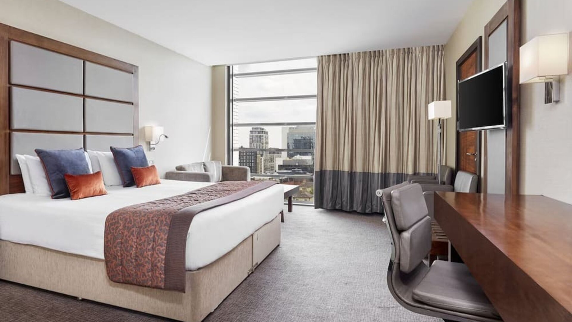 Day use room with TV, work desk and floor to ceiling windows with view of the city at Leonardo Royal Hotel London Tower Bridge.