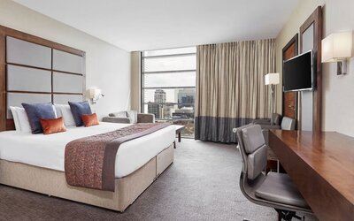 Day use room with TV, work desk and floor to ceiling windows with view of the city at Leonardo Royal Hotel London Tower Bridge.