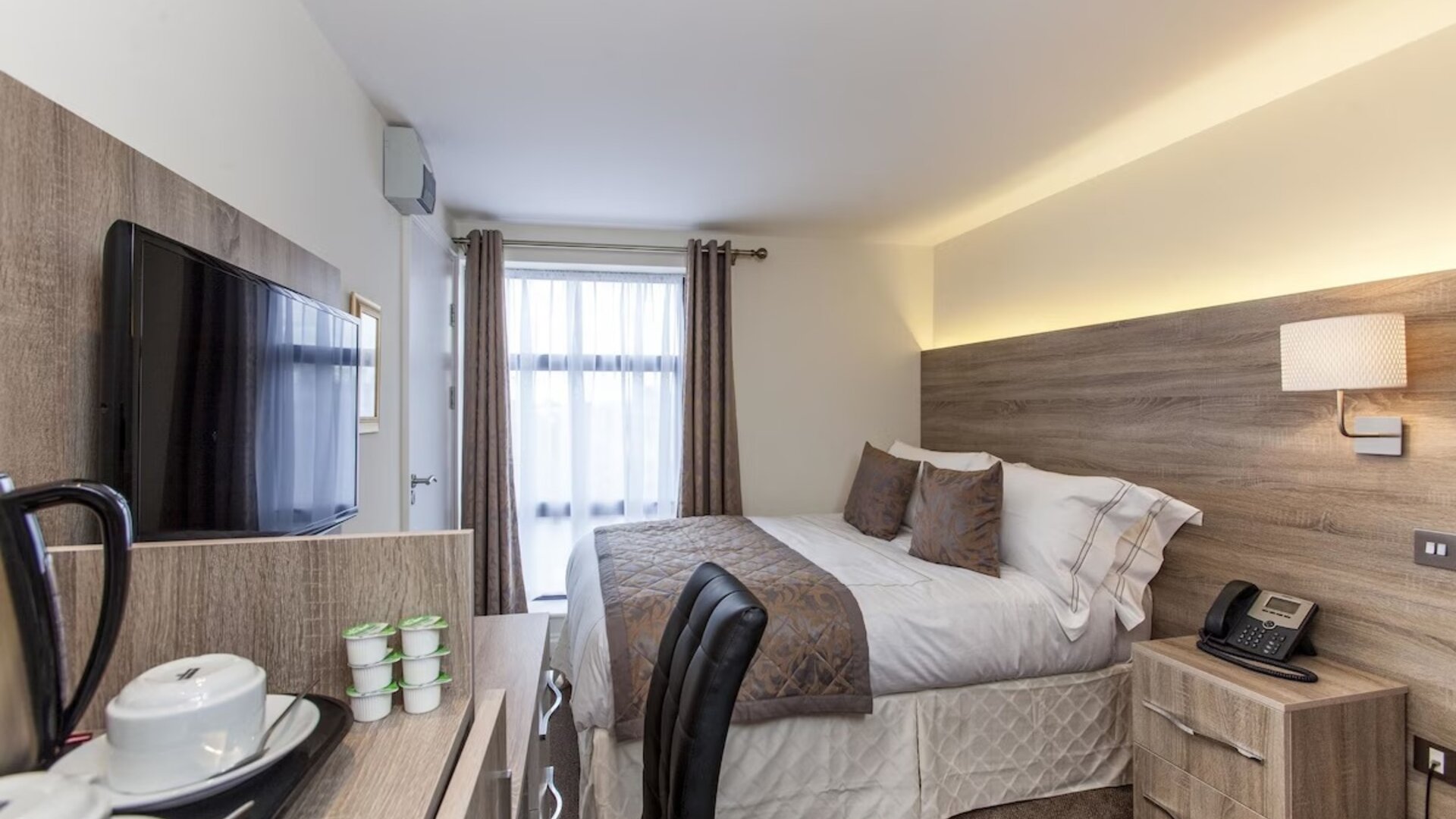 Day use room with work desk, TV screen, floor to ceiling window and coffee station at Hotel Shepherds Bush London.
