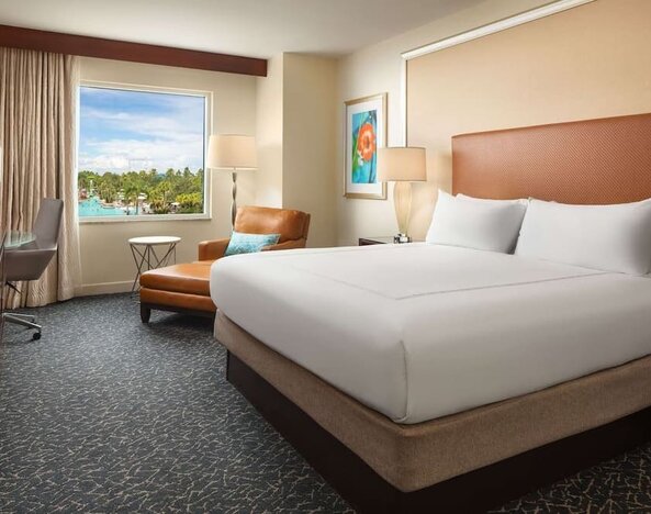 King room with TV, work desk, sofa and a great pool view at Hilton Orlando.