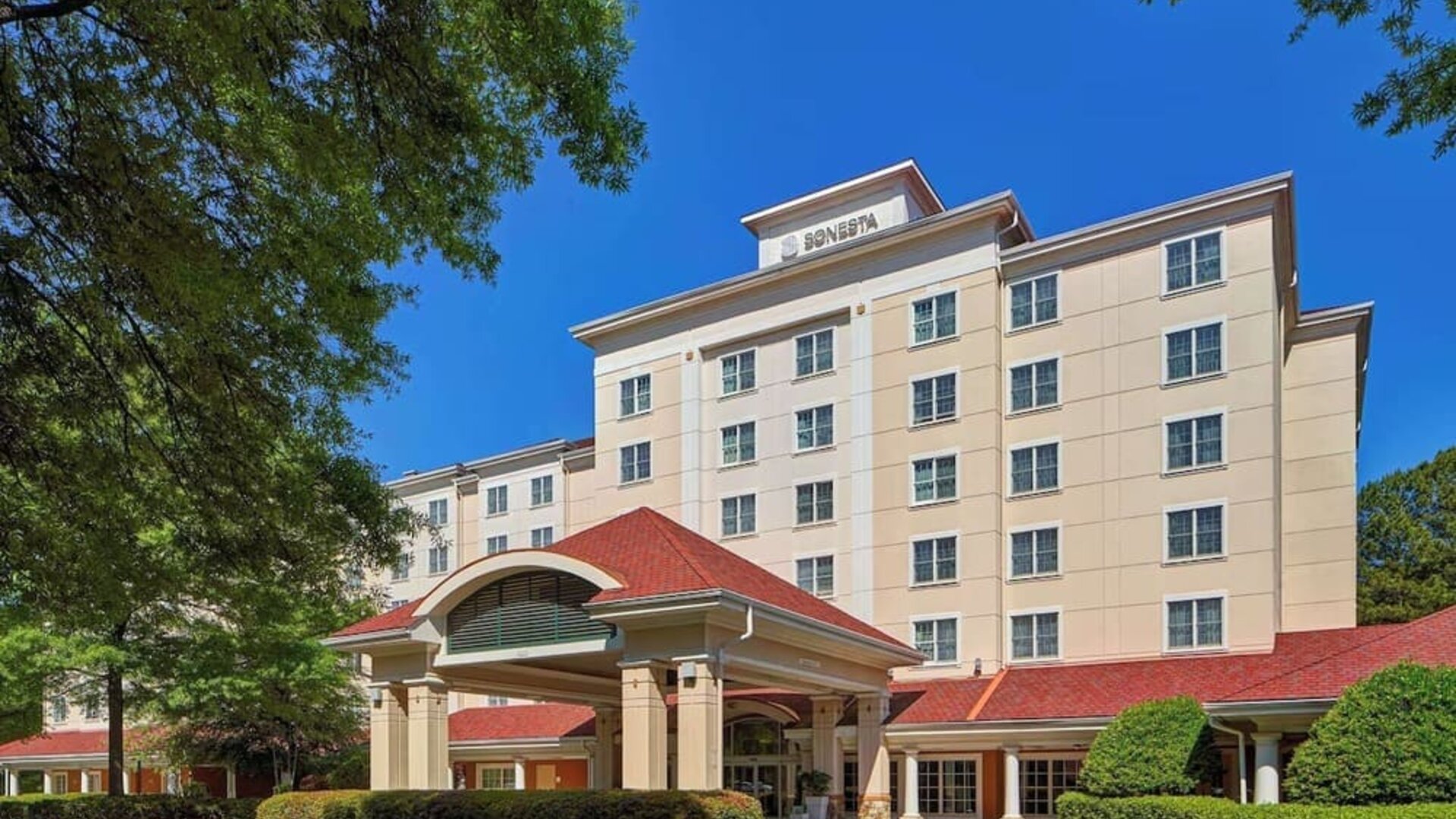 Sonesta Atlanta Airport South’s exterior features a covered entrance, well-kept greenery, and stylish red roof tiles.