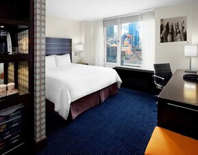 King bedroom with TV, work station and a view of the city at Hilton New York Fashion District.