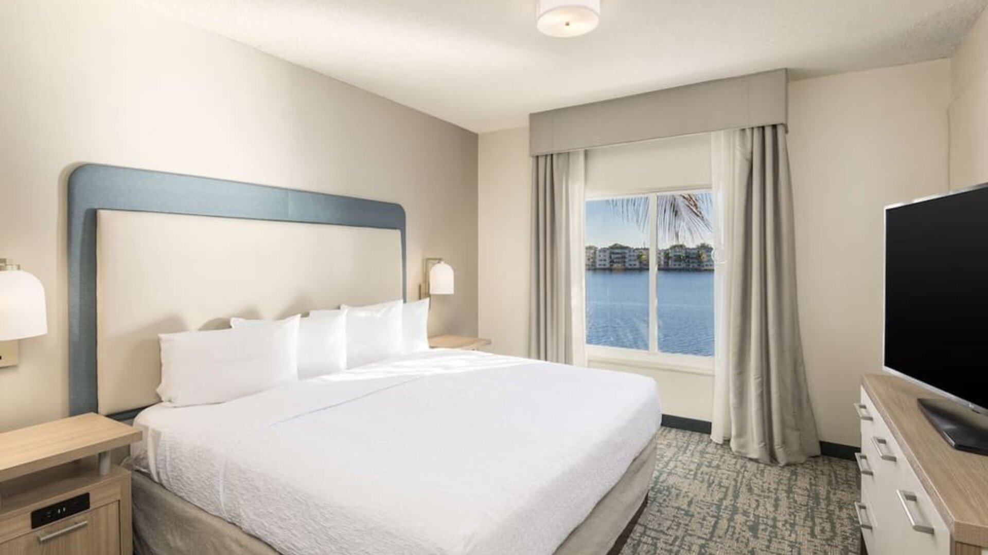 King bed with TV and a view of the Blue Lagoon at Homewood Suites By Hilton Miami Airport-Blue Lagoon.