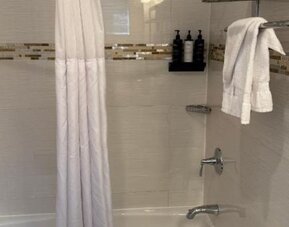 Bathroom at Madison LES Hotel with bathtub and shower with privacy curtains and towels.