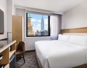 Guest room in the DoubleTree Times Square South, with a bed, beautiful view of the city and workspace desk and chair.
