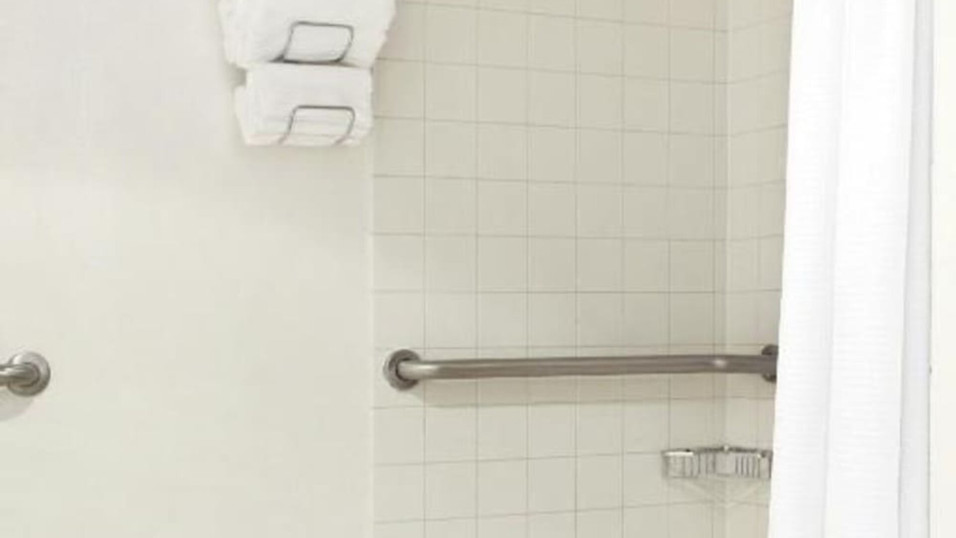 Bathroom with tiled walk-in shower, grab bar, mounted towels, and curtain at Renaissance Newark Airport Hotel.