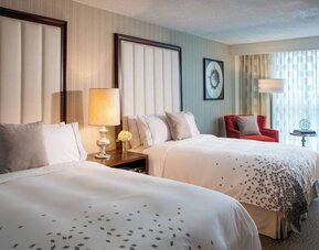 Guest room with two beds, bedside table, lamp, armchair, and window with curtains at Renaissance Newark Airport Hotel.