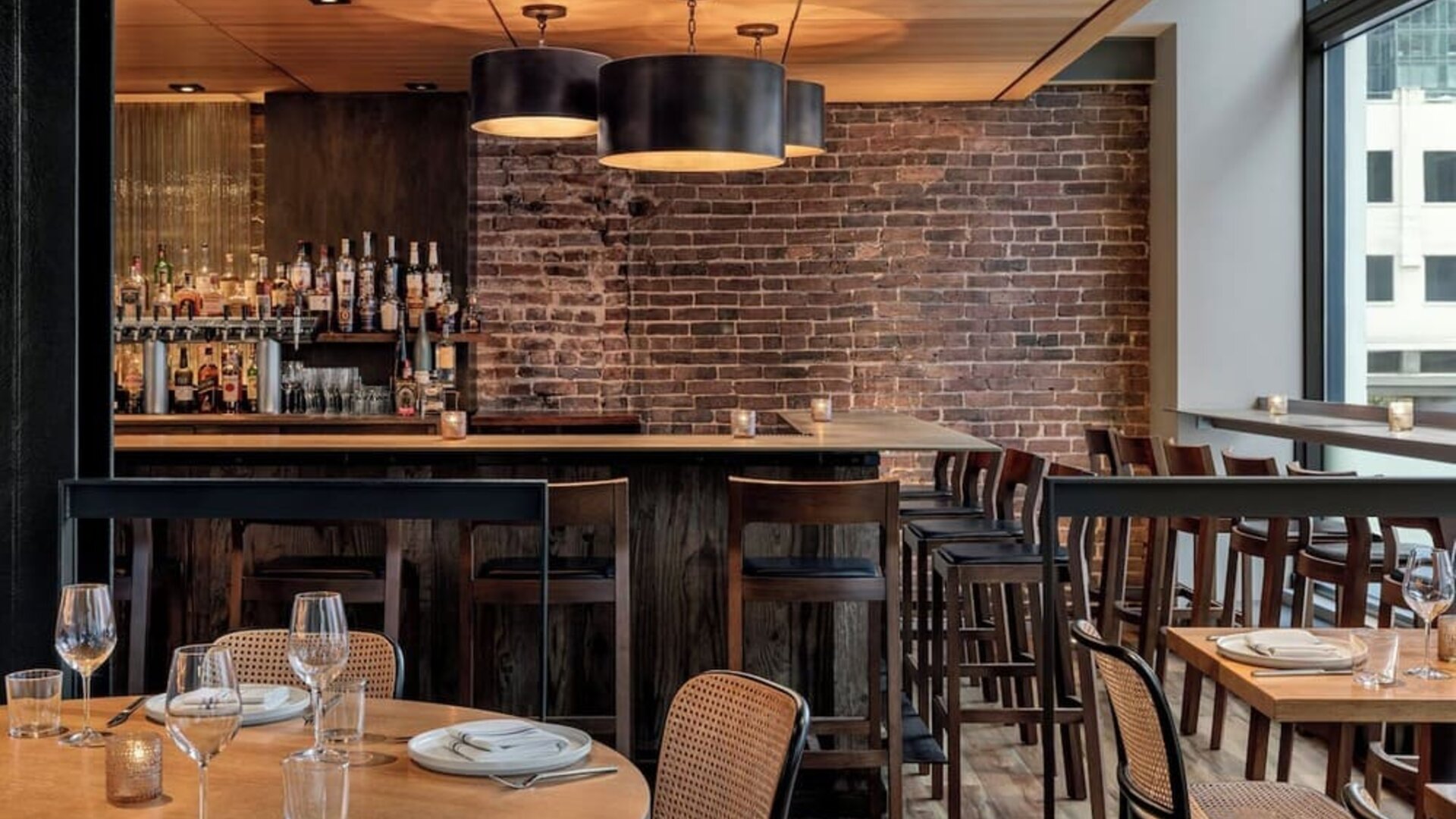 Restaurant dining area with wooden tables, chairs, bar seating, and brick wall at Kimpton Palladian Hotel.