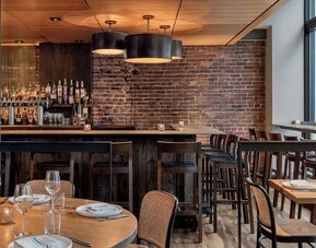 Restaurant dining area with wooden tables, chairs, bar seating, and brick wall at Kimpton Palladian Hotel.
