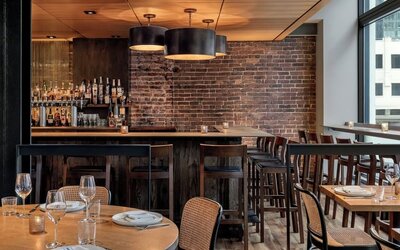Restaurant dining area with wooden tables, chairs, bar seating, and brick wall at Kimpton Palladian Hotel.