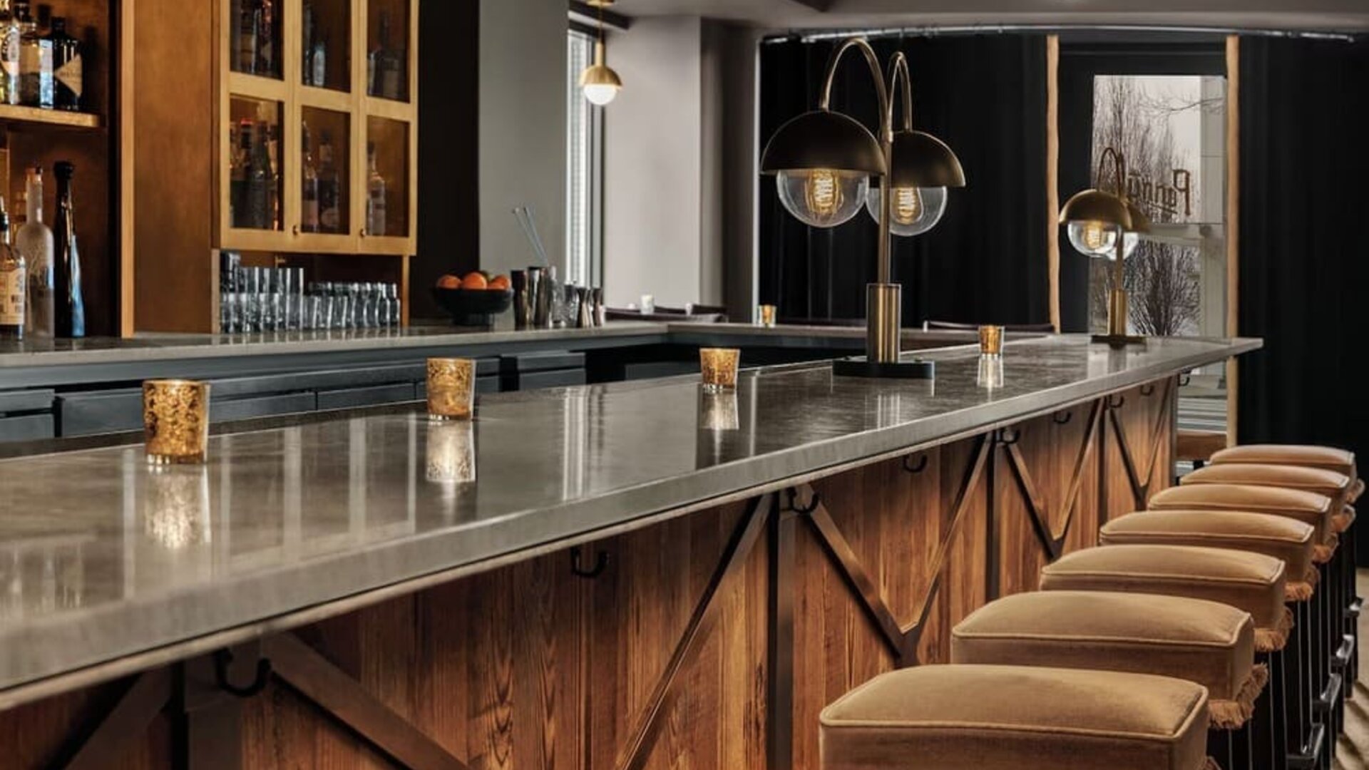 Long marble bar counter with upholstered stools, pendant lighting, and liquor shelves at Kimpton Palladian Hotel.