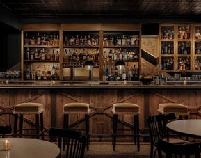 Bar interior with wooden counter, cushioned stools, shelves, and glassware at Kimpton Palladian Hotel.