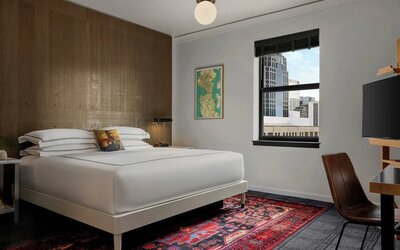 Guest room with king bed, wood accent wall, desk, chair, and patterned rug at Kimpton Palladian Hotel.