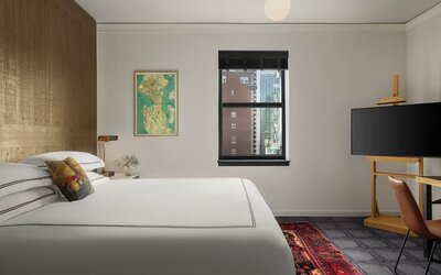 Bright bedroom with king bed, dual windows with city buildings, and framed artwork at Kimpton Palladian Hotel.