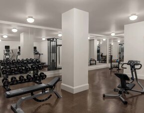 Spacious gym with dumbbells, benches, resistance equipment, and mirrors at Kimpton Palladian Hotel.