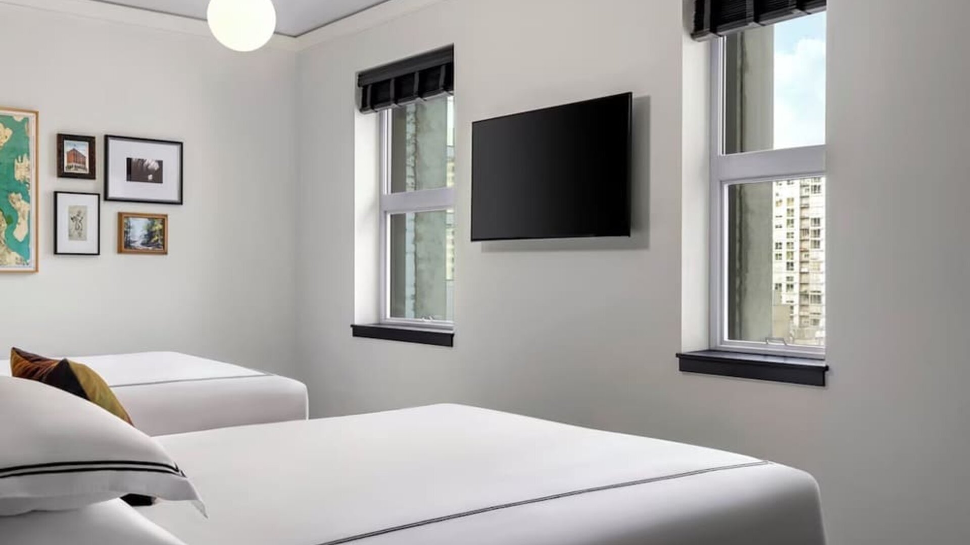 Twin bedroom with two beds, framed artwork, wall-mounted TV, and natural light at Kimpton Palladian Hotel.