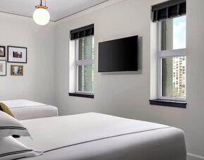 Twin bedroom with two beds, framed artwork, wall-mounted TV, and natural light at Kimpton Palladian Hotel.