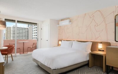 Spacious guest room with bed, seating area, and balcony access at The Ambassador Hotel Of Waikiki.