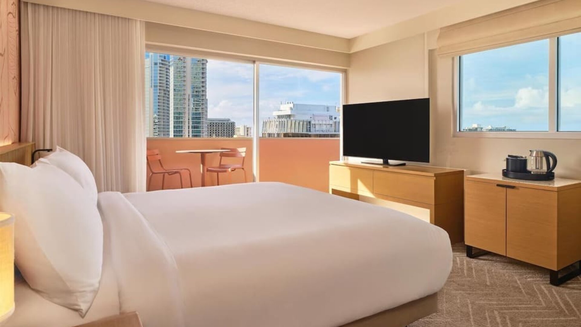 Bright guest room with large windows, bed, and TV console at The Ambassador Hotel Of Waikiki.