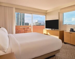 Bright guest room with large windows, bed, and TV console at The Ambassador Hotel Of Waikiki.
