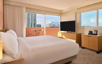 Bright guest room with large windows, bed, and TV console at The Ambassador Hotel Of Waikiki.